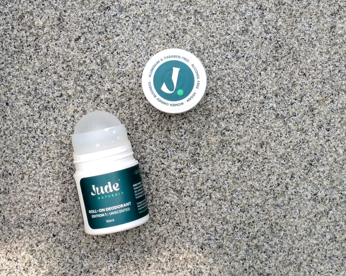 Close-up of open bottle displaying 50ml bottle of Jude Naturals Unscented natural roll-on deodorant. Live background on stone surface. 