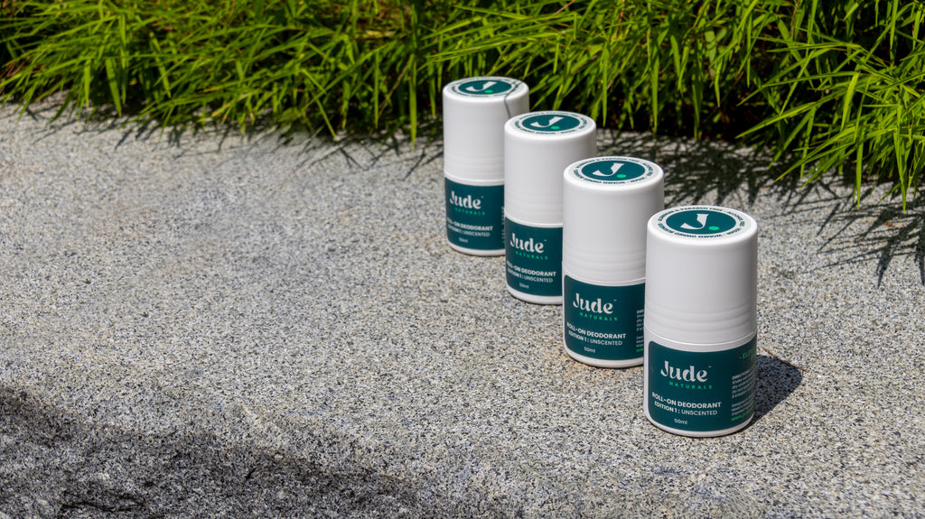 A row of 50ml bottle of Jude Naturals Unscented natural roll-on deodorant. Live background on stone surface with greenery in the back. 
