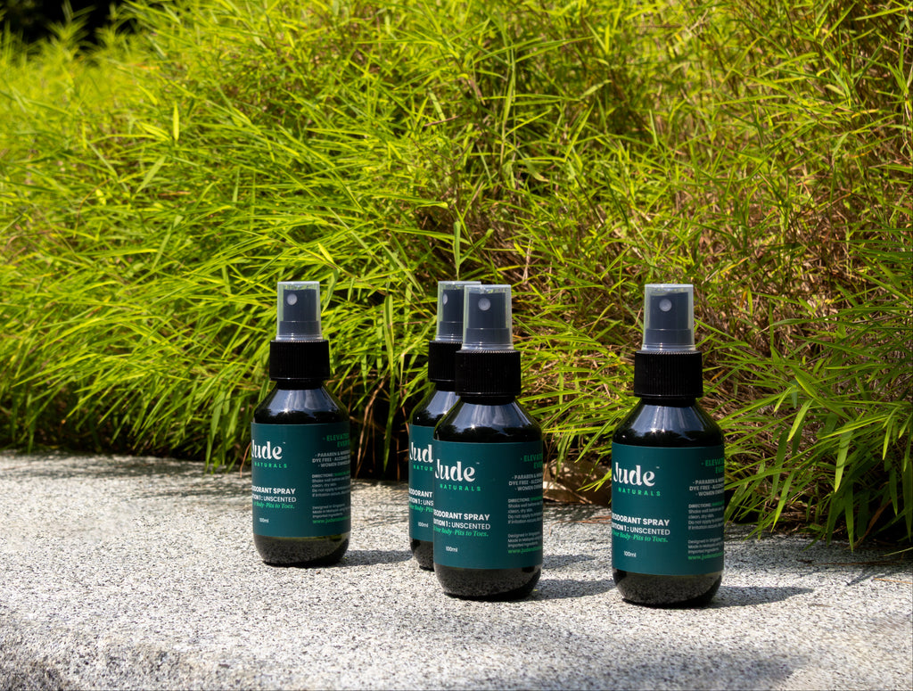 Row of 100ml Jude Naturals spray deodorant with mineral salt formula with live background of greenery and stone surface. 