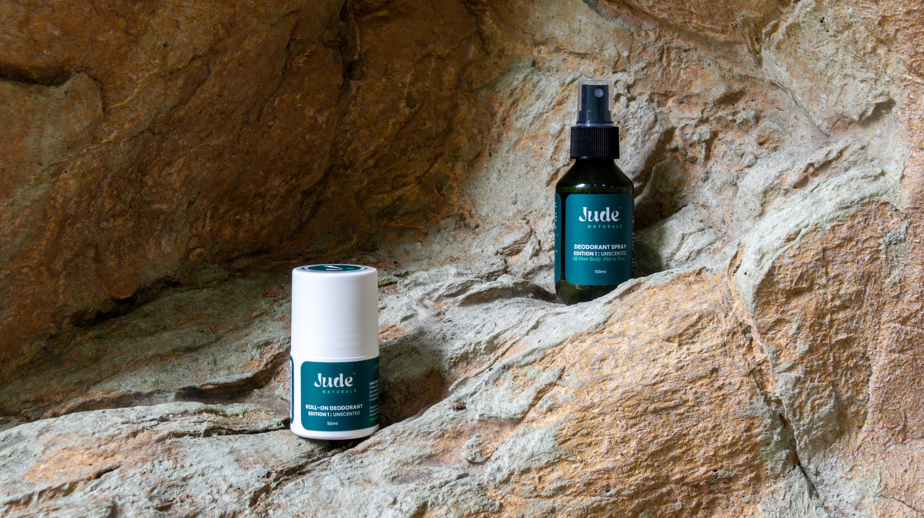 Jude Naturals deodorant bundle set with 100ml spray and 50ml roll-on, edition 1 unscented set on natural rock surface background. 